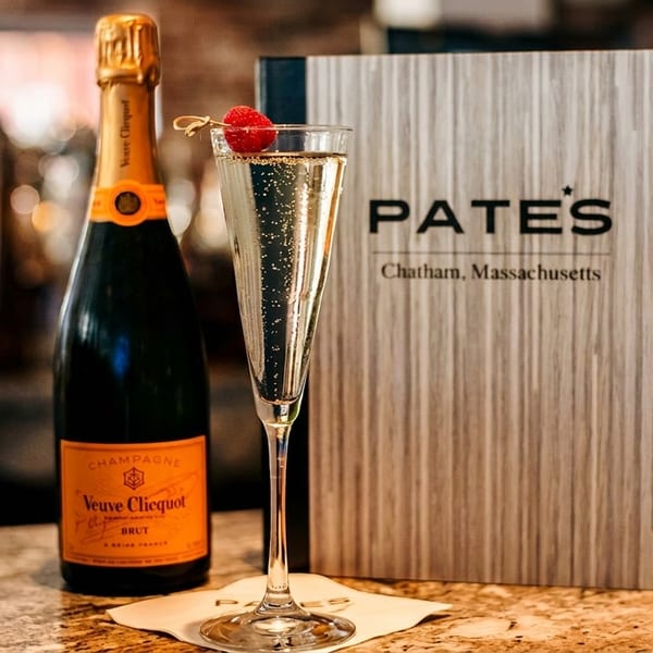 A bottle of Veuve Clicquot champagne, a flute, and a Pate's restaurant menu on a bar.