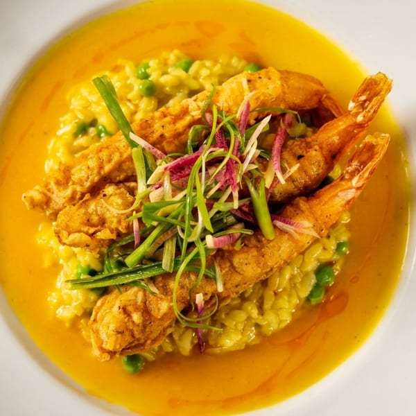 Crispy fried shrimp over yellow risotto with peas, scallions, and red radish in a rich sauce.