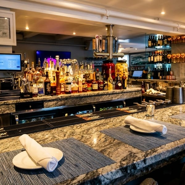 A well-stocked bar with bottles of liquor, wine, and beer taps, featuring a granite countertop with place settings.