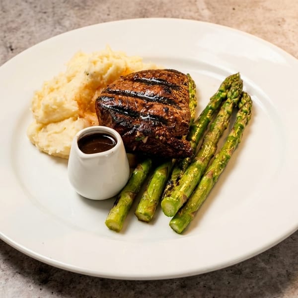 Grilled steak with mashed potatoes, asparagus, and a side of gravy on a white plate.