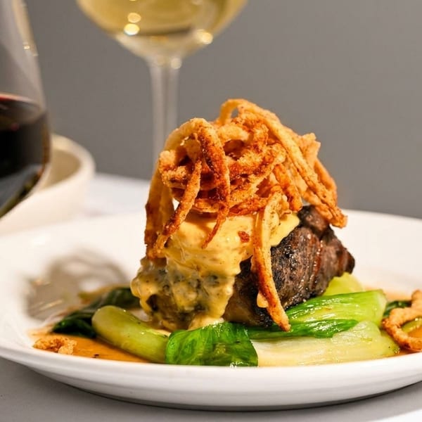 Steak with sauce and crispy fried onions on bok choy, with a glass of red wine.
