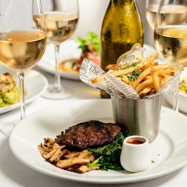 A table set with multiple plates of food, including steak, fries, and chicken, with wine glasses.